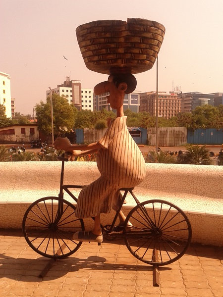 Sculpture o woman on bicycle with a large basket on her head in Goa, India